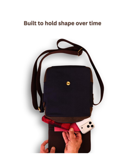 A navy blue and brown crossbody bag with a gold snap button, shown with a phone and wallet partially pulled out from the bottom pocket. Text at the top reads 'Built to hold shape over time' on a white background.