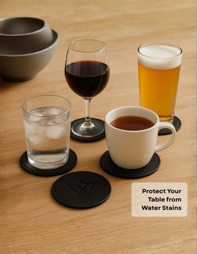 Black circular silicone coasters shown on a wooden table with various drinks, including a glass of red wine, a glass of beer, a glass of water, and a white mug of tea. A text overlay in the bottom right corner reads 'Protect Your Table from Water Stains'.