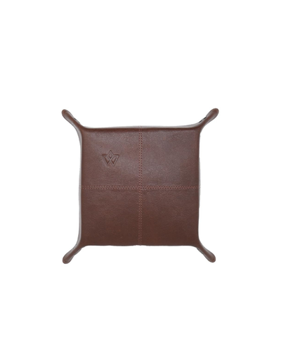 A square brown leather throw pillow with four curved legs and a debossed logo on the front, shown against a plain white background.