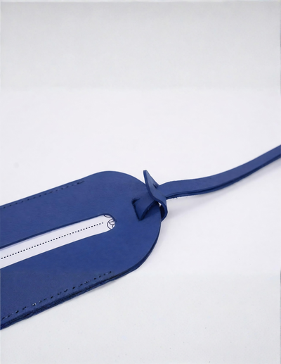 A blue leather luggage tag with a white printed barcode slot and a matching blue strap, photographed on a clean white background.