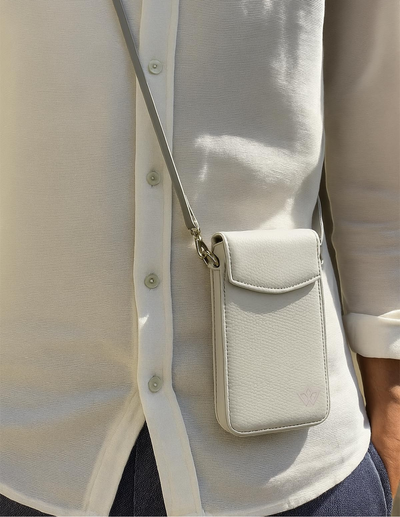 A close-up of a person wearing a white button-up shirt and dark pants, carrying a small off-white textured crossbody phone pouch with a silver strap.