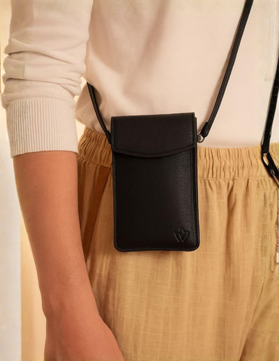A black leather crossbody phone pouch with a small embossed logo, worn by a model in a cream ribbed long-sleeve top and beige trousers.