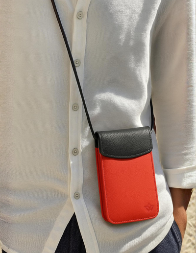 A close-up of a person wearing a white button-up shirt and dark pants, carrying a small red and black crossbody pouch bag on a black strap.