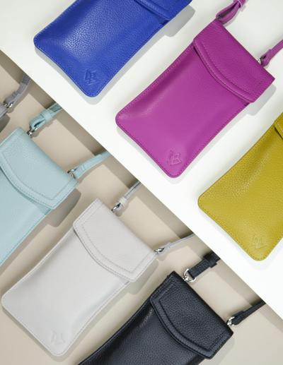 Six pebbled leather pouches in blue, purple, light blue, white, black, and yellow, arranged diagonally on a white shelf.