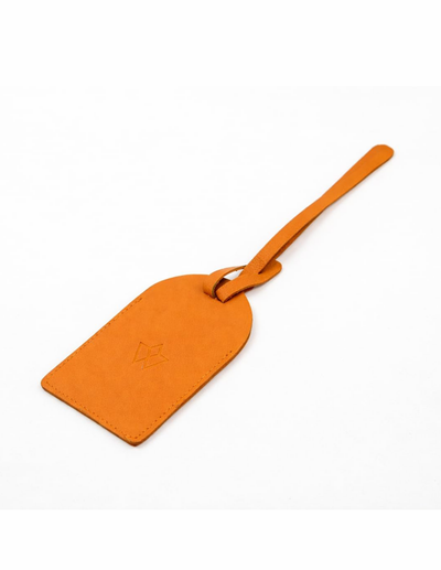 An orange leather luggage tag with a matching loop strap, featuring an embossed geometric logo on the front, set against a plain white background.
