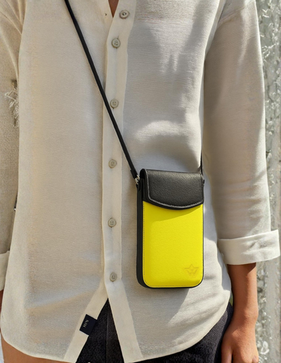 A person wearing a white button-up shirt carries a small crossbody phone pouch with a bright yellow body and a black flap and strap.
