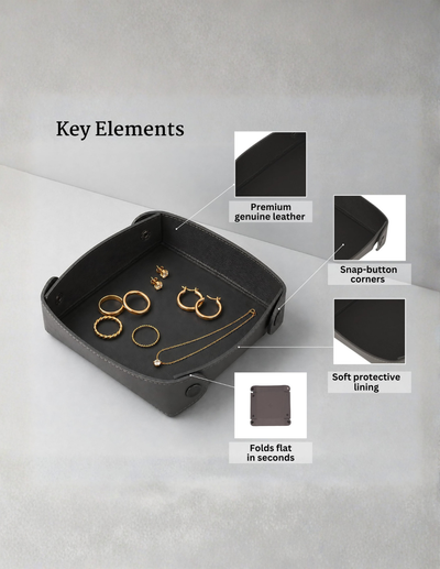 A black leather jewelry organizer tray with gold jewelry displayed inside, shown on a light gray background with callout labels pointing to key features: premium genuine leather, snap-button corners, soft protective lining, and folding capability.