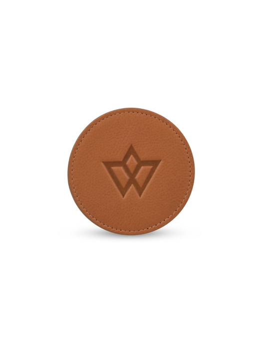A round brown leather accessory with a debossed geometric logo in the center, shown on a clean white background.