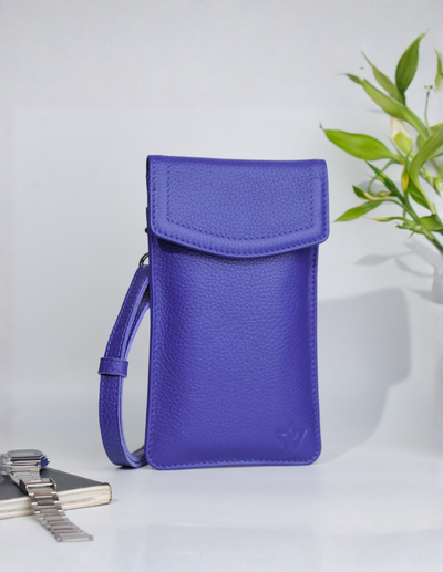 A vibrant purple pebbled leather crossbody phone pouch with a matching wrist strap, standing upright on a white surface with a watch and green leaves as props.