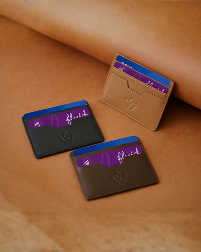 Three slim card holders in tan, dark brown, and black leather, each with a purple card in the slot, arranged on a tan leather surface with a matching curved prop.